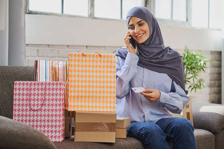 Young Arabian lady holding a card, talking on the phone and looking at giftsの写真素材