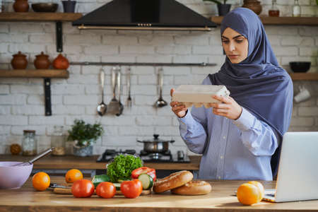 Young Arabian woman holding a tray with eggs and reading the label attentivelyの写真素材