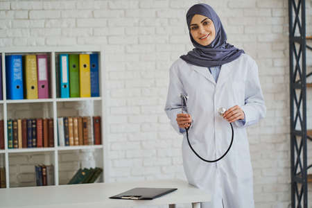 Friendly Muslim doctor posing with a stethoscope near her workplaceの写真素材