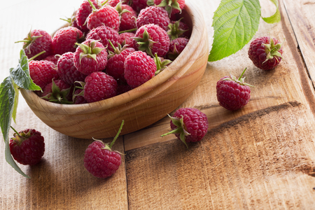 raspberries in wooden plate on the wooden background.