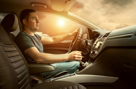 Man sitting and driving in the car under sunset sky