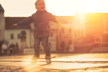 Child with skateboard on the street at sunset light.の写真素材