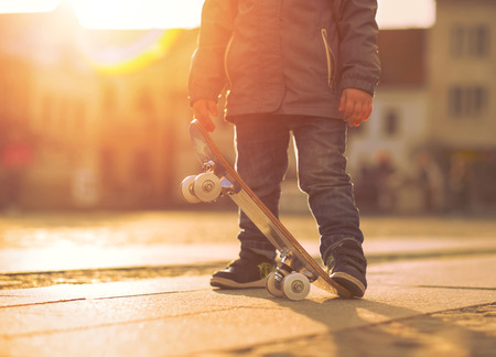 Child with skateboard on the street at sunset light.の写真素材