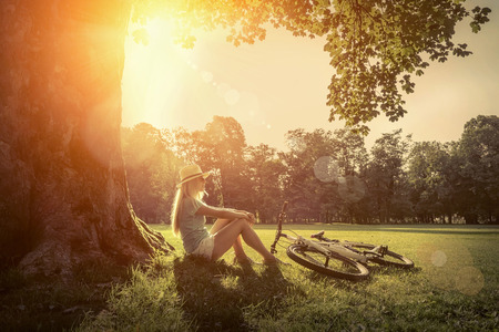 Woman sitting under sun light at day near her bicycle in the park