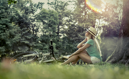 Woman sitting under sun light at day near her bicycle in the parkの写真素材