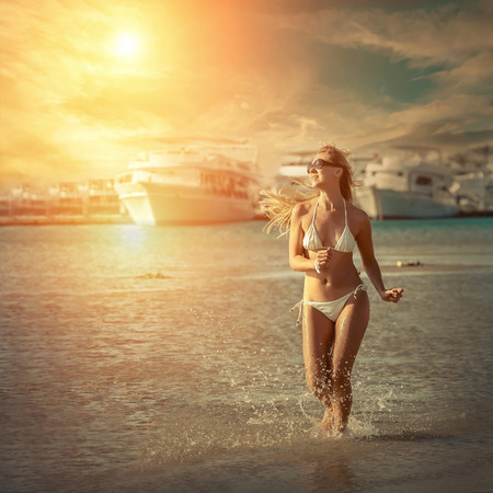 Happiness female running on the beach, yachts background and under sunlightの写真素材