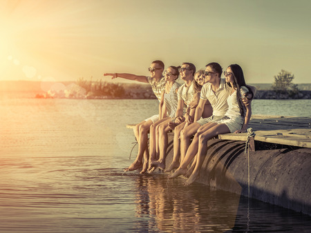Friends sitting on wooden pier under sunset light.の写真素材