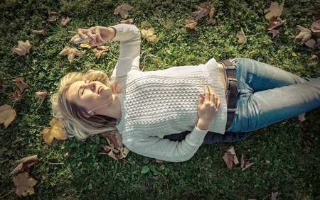 Woman listening music on grass at autumn timeの写真素材