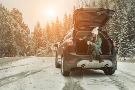 Woman at winter time. Yoyng female with hot tea in her hands sitting in black car at snowly winter day.の写真素材