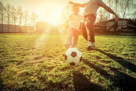 Father and son playing together with ball in football under sun light. Green field in city park at sunny day.の写真素材