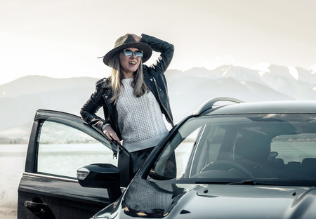 Woman at spreeng time. Yoyng happines female in hat and sunglasses stay near her black car at sunny...
