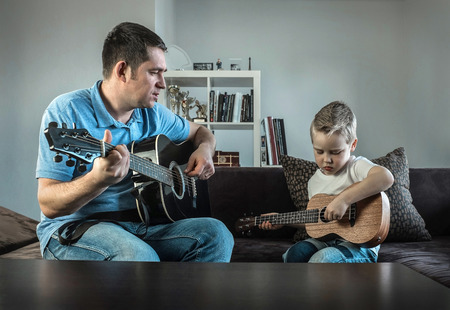 Father teaching his son to play on guitar at home. Son play on ukulele - hawaiian guitar.の写真素材