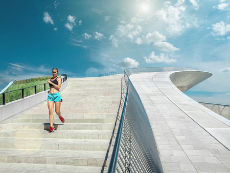Blonde woman running training near the modern architecture building. Sport. Run. Blue sky. Sunny...