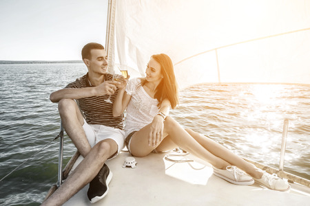 Romantic couple in love on sail boat drinking wine under sunset  sunlight on yacht - Happy exclusive alternative lifestyle concept - Love story of two caucasian young people.の写真素材