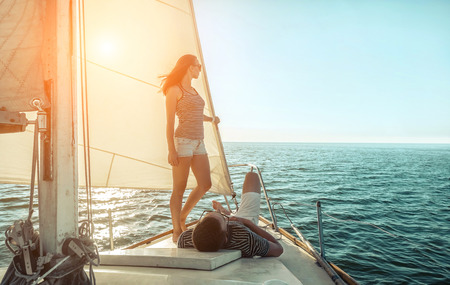 Romantic couple in love on sail boat at sunset under sunlight on yacht - Happy exclusive alternative lifestyle concept - Love story of two caucasian young people.の写真素材