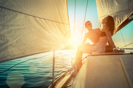 Romantic couple in love on sail boat at sunset under sunlight on yacht - Happy exclusive alternative lifestyle concept - Love story of two caucasian young people.の写真素材