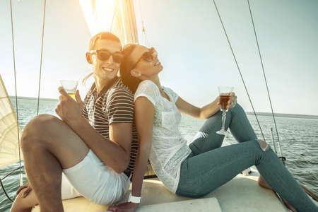 Romantic couple in love on sail boat drinking wine under sunset  sunlight on yacht - Happy exclusive alternative lifestyle concept - Love story of two caucasian young people.の写真素材