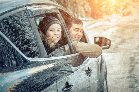 Happiness caucasian smilling boy with his father looking out of black car window in sunny day at winter time near the forest.の写真素材