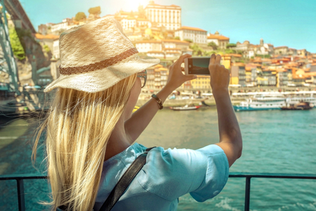 Happy blonde woman - tourist shot on her smartphone camera beautiful city view. with ships on the river in sunny day.の写真素材