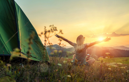 Happy woman with open arms stay near tent around mountains under sunset light sky enjoying the  leisure and freedom.の写真素材