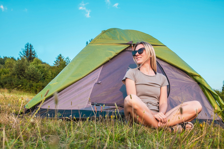 Happy woman with open arms sitting near tent around mountains under sunset light sky enjoying the  leisure and freedom.の写真素材