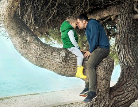 Happy childhood, father and son sit on a tree on a sunny day, family vacationsの写真素材