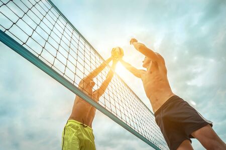 Beach Volleyball players in sunglasses in action with ball under sunlight. Popular Dynamic outdoor sport for people.の写真素材