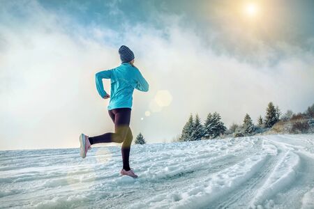Running woman. Runner on the snow in winter sunny day. Female fitness training outdoors.の写真素材