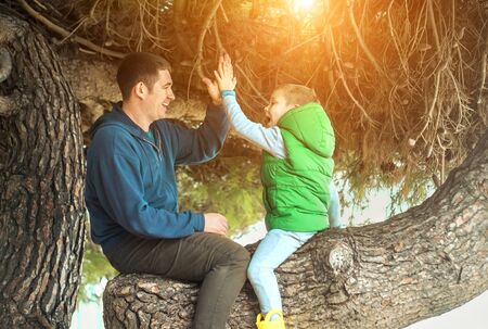 Happy childhood, father and son sit on a tree on a sunny day, family vacations