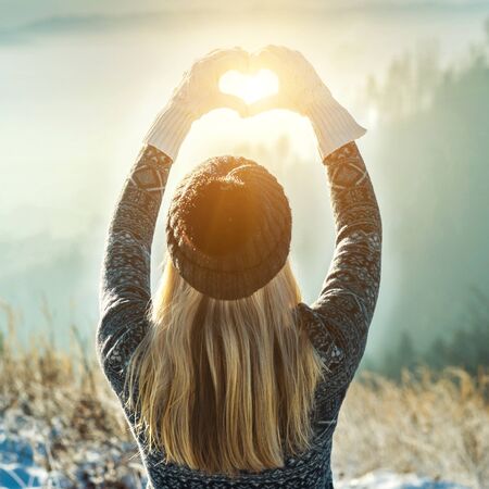 Happy traveler woman tourist stay on mountain top and making of love heart by hands in sunny frozen...