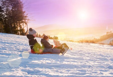 Children ride from a snow slide, have fun, play. Happy winter holidays.