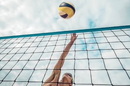 Beach Volleyball player in sunglasses in action with ball under sunlight. Popular Dynamic outdoor sport for people.の写真素材