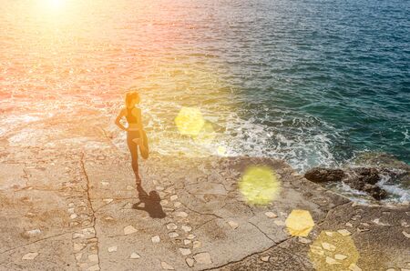 Woman running training on the coastline under sunlight in sunny summer dayの写真素材