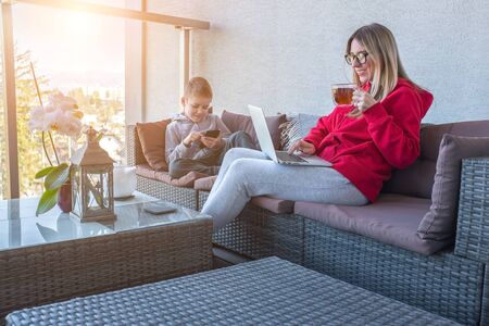 Stay at home mom. Mother and son spend free time on terrace. Woman working, child using smartphone. Weekend Family. Bonding concept.の写真素材