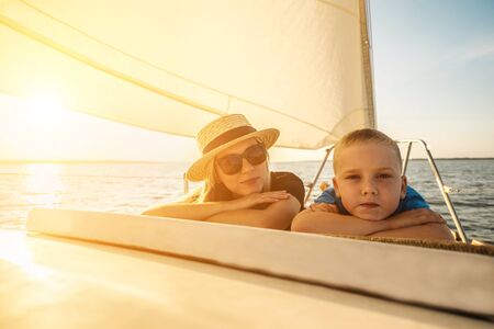 Happy traveler mother and son enjoying sunset from deck of sailing boat moving in sea at evening...