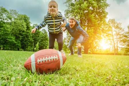 Father and son playing football, Father's day, Playful Man teaching Boy rugby outdoors in sunny day...
