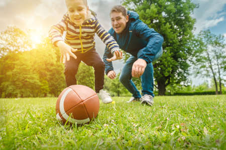 Father and son playing football, Father's day, Playful Man teaching Boy rugby outdoors in sunny day at public park. Family sports weekend.の写真素材