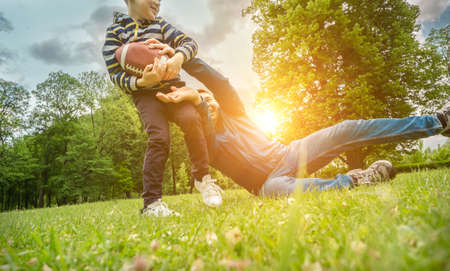 Father and son playing football, Father's day, Playful Man teaching Boy rugby outdoors in sunny day at public park. Family sports weekend.の写真素材