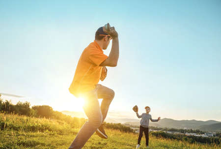 Father and son playing in baseball. Playful Man teaching Boy baseballs exercise outdoors in sunny day at public park. Family sports weekend. Father's day.の写真素材