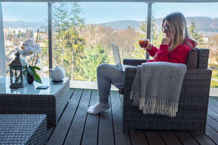Stay at home, working in house. Woman spend free time on terrace in home clothes. Work with laptop...