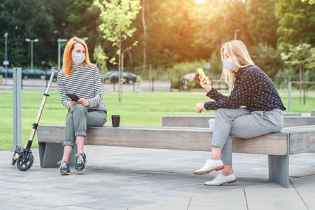 Female colleagues entrepreneurs wearing masks working over tablet, while sitting on seat in town. Woman faces wearing masks. Long distance communication. Staying connectedの写真素材