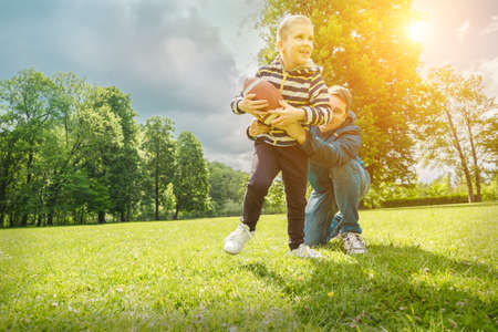 Father and son playing football, Father's day, Playful Man teaching Boy rugby outdoors in sunny day at public park. Family sports weekend.の写真素材