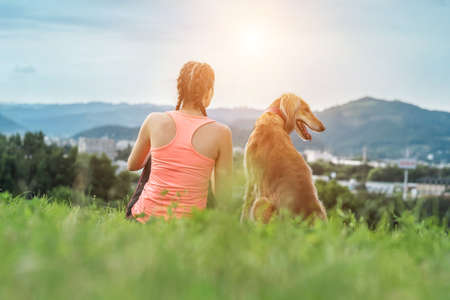 Woman runner and dog on field under golden sunset sky in evening time. Outdoor running. Athletic young man with his dog are running in nature.の写真素材