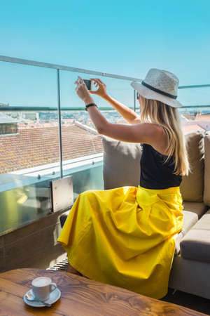 Young traveler woman with smartphone sitting cafe in Lisbon and takes pictures of the city.の写真素材