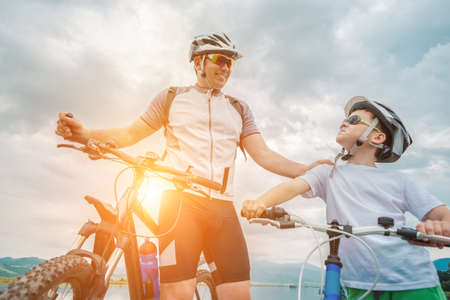 Father and son ride, cycling their bikes together, on sunny day, Happy family in helmets is riding bikes having fun.の写真素材