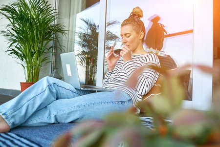 Working from home. Woman talking on video call with Family, using laptop and drinking tea. Online chat. Spend free time on terrace. Staying connected, Social distancing, internet, chatting.の写真素材
