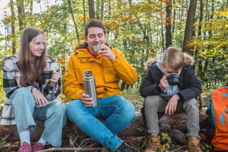 Father and children resting in nature, drinking hot tea a thermos in sunny autumn day.の写真素材