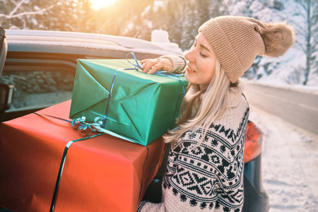Woman Giving Gifts. Female is holding presents and delivering them on her car to Home. Holidays concept. Driving car in Christmas Eve. People In A Snow-Covered Forest. Sunny Cold Winter Day.の写真素材