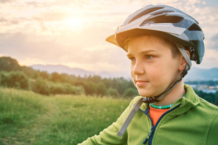 Mother teaching son to ride bicycle. Happy cute boy in helmet learn to riding a bike in park on green meadow in summer day at sunset time. Family weekend. 4K video Slow motionの写真素材