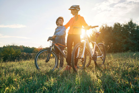 Mother and son ride a bike. Happy cute boy in helmet learn to riding a bike in park on green meadow in autumn day at sunset time. Family weekend. 4K video, Slow motionの写真素材